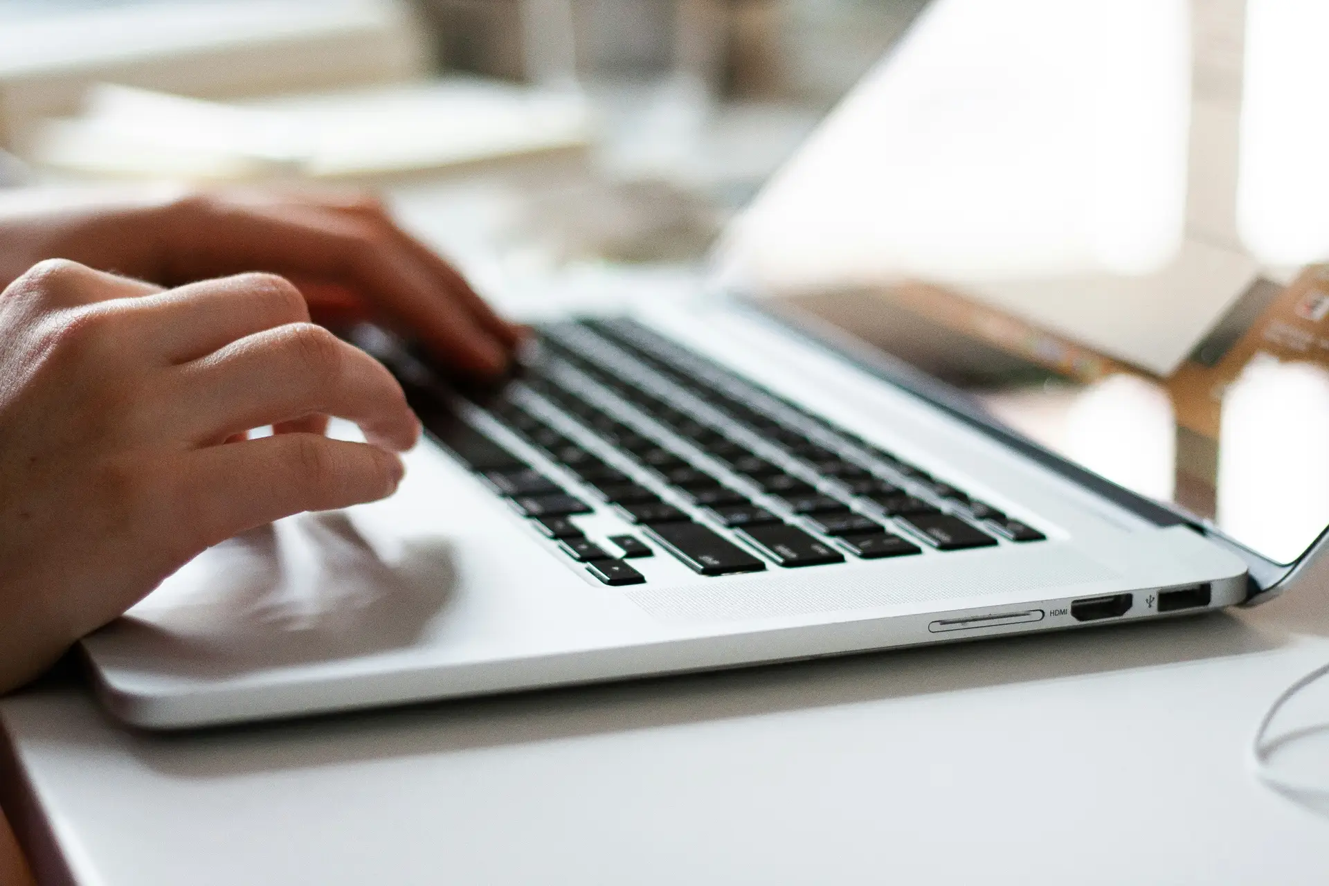 Hände tippen auf einer Laptop-Tastatur neben Notizbuch mit handschriftlichen Korrekturen