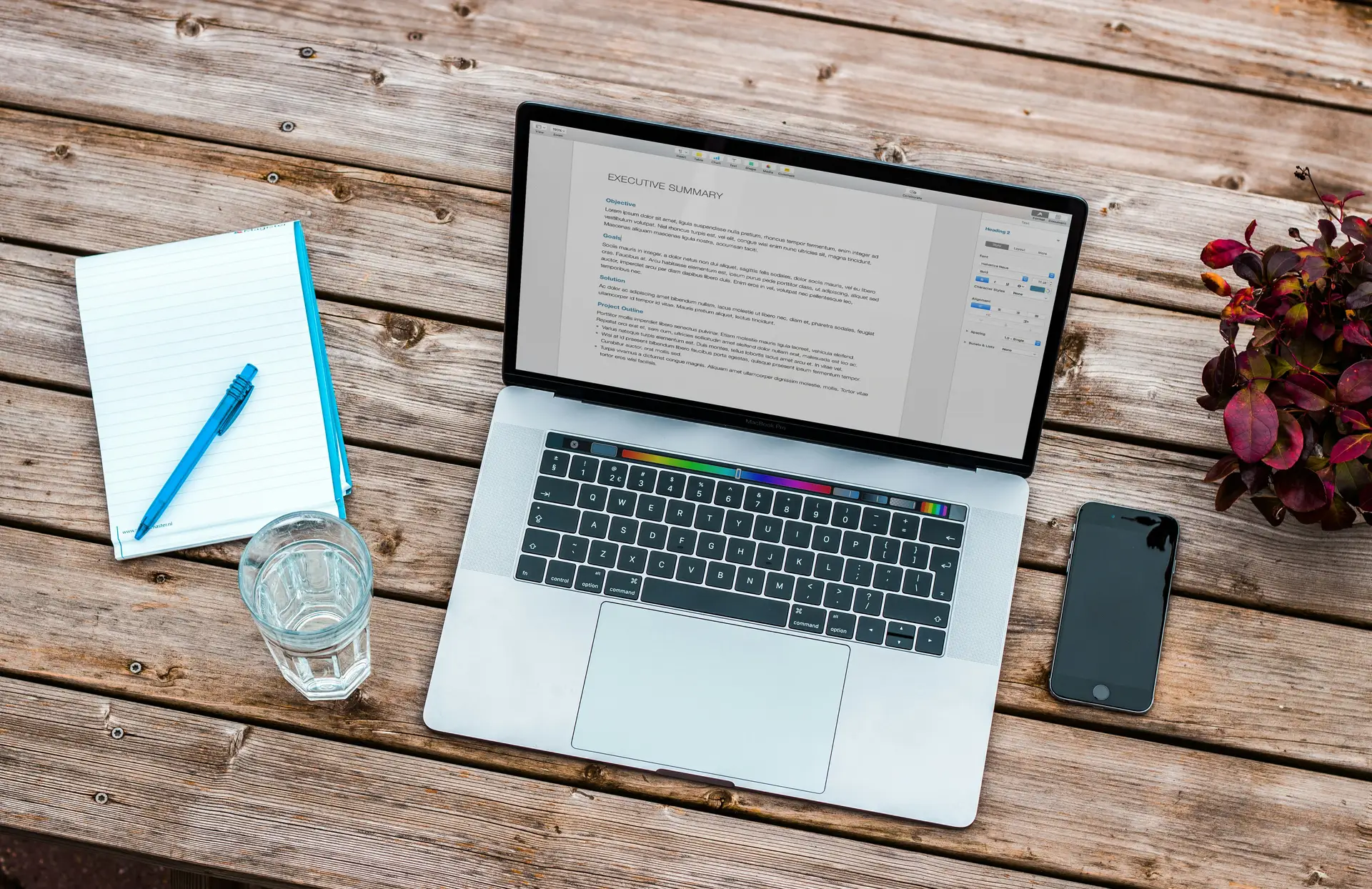 Laptop mit geöffnetem Textdokument und markierten Korrekturvorschlägen, daneben Notizbuch und Kaffeetasse